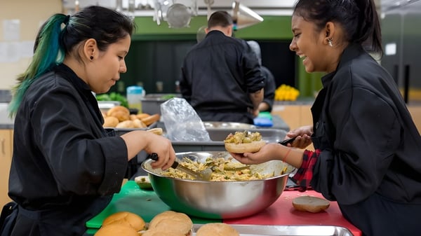 Dos estudiantes de la École des Sept Sommets sirven comida de un gran cuenco mientras otras personas están en el fondo.