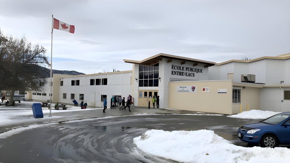 Una bandera canadiense ondea frente a un paisaje nevado en el terreno de la École Entre-Lacs.