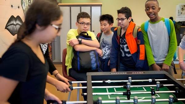 Estudiantes de la École Gabrielle-Roy juegan juntos en una mesa de futbolín en el edificio escolar.