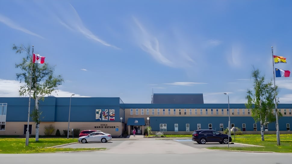 El moderno edificio de varios pisos de la École Marie-Esther está rodeado de un prado con árboles y coches estacionados.