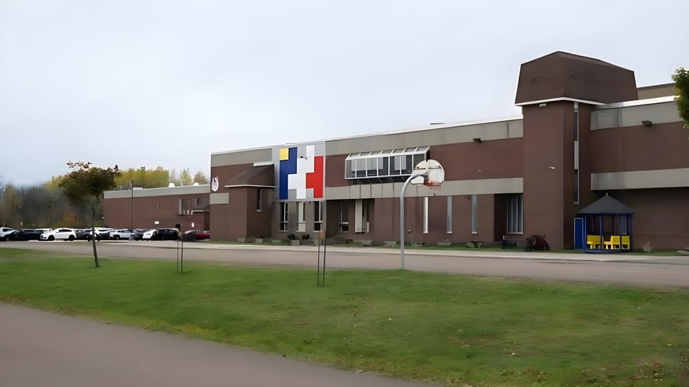 El moderno edificio de varios pisos de la École Mathieu-Martin se encuentra en un área de césped con una canasta de baloncesto en primer plano.