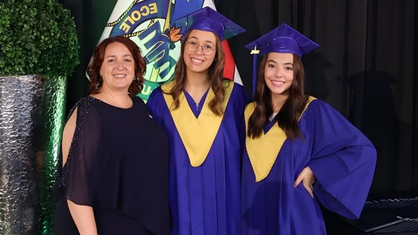 Tres alumnas de la École Mathieu-Martin en ropa de graduación posan frente a un fondo verde con el logo de la escuela.