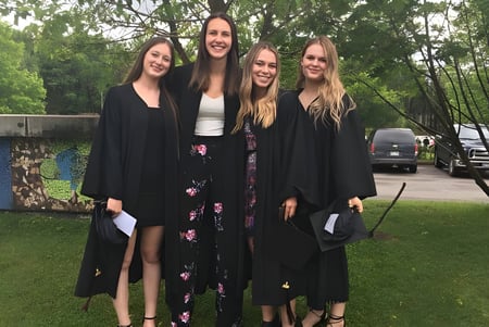 Cuatro estudiantes están juntos al aire libre sobre el césped de la École Polyvalente Secondaire Curé-Mercure frente a una pared de graffiti.