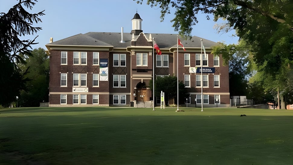 El edificio de ladrillo de varios pisos con reloj en el terreno de la École secondaire publique Rivière Rideau está rodeado de árboles y un prado.