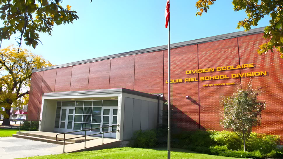 El edificio de ladrillo de la École secondaire publique Louis-Riel está rodeado de árboles y una superficie de césped.