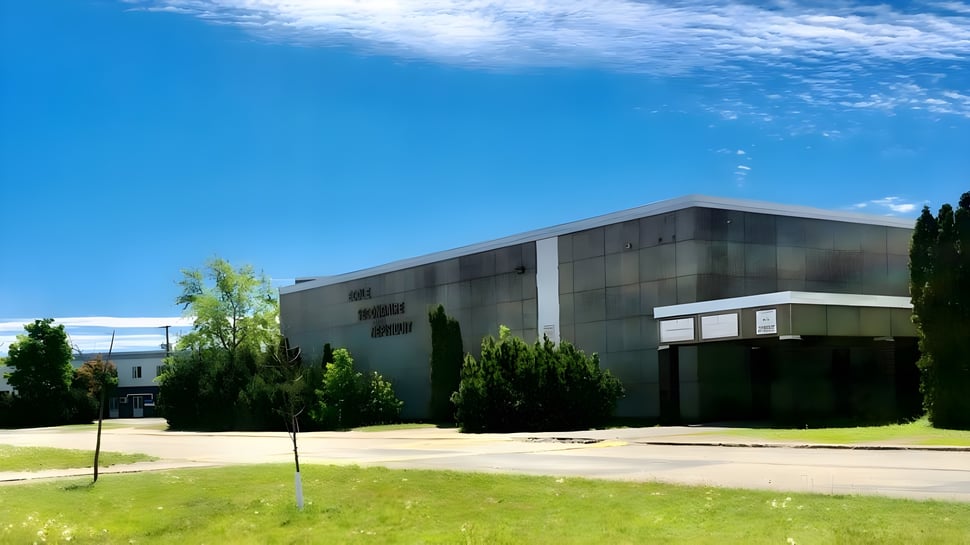 El moderno edificio de varios pisos de la École secondaire Népisiguit con fachada de vidrio se encuentra en un paisaje verde bajo un cielo azul.