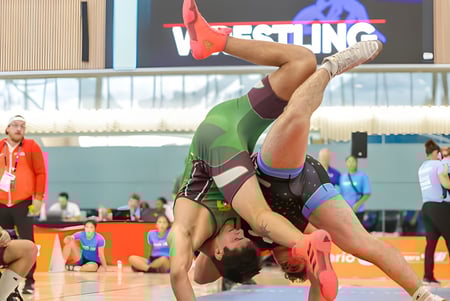 Una luchadora en uniforme rojo y verde realiza un movimiento acrobático en la colchoneta durante una competencia de la École secondaire Népisiguit.
