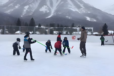 Estudiantes de la École Sophie Morigeau patinando sobre una pista congelada frente a un paisaje montañoso nevado.
