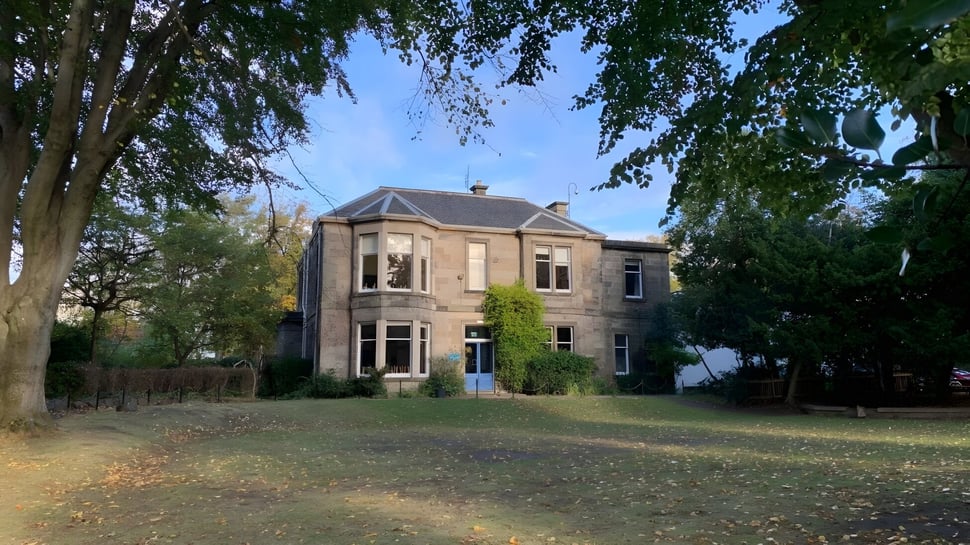 El edificio de ladrillo de la Edinburgh Steiner School está rodeado de árboles y hojas otoñales en el terreno escolar.
