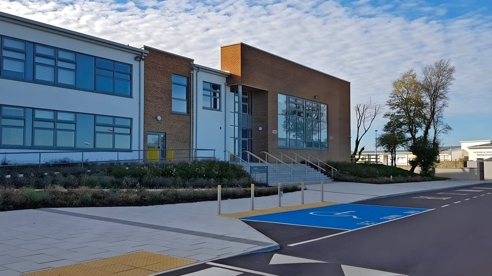 El moderno edificio de varios pisos del Edmund Rice College con grandes ventanas y un área pavimentada azul y amarilla en primer plano.