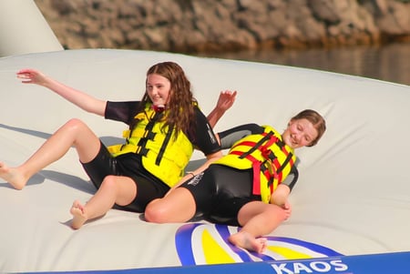Dos alumnas del Edmund Rice College están sentadas con chalecos salvavidas en una balsa blanca frente a juncos.