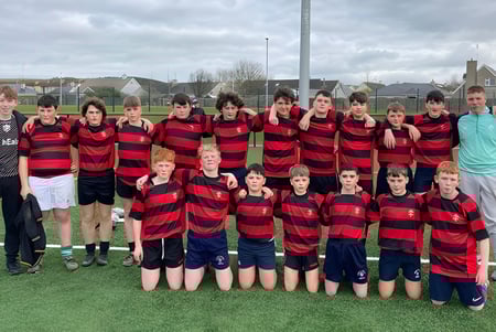 Un grupo de estudiantes de la Edmund Rice Secondary School está en un campo deportivo con camisetas a rayas rojas y negras.