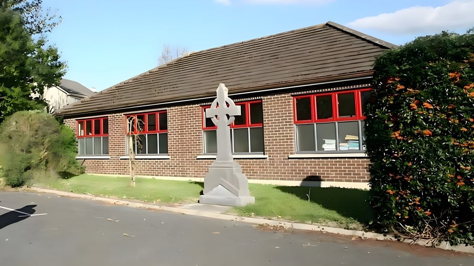 El edificio de ladrillo de la Edmund Rice Secondary School está rodeado de árboles con una estatua en primer plano.