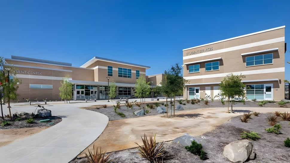El moderno edificio de varios pisos de la El Cajon Valley High School con un patio verde y camino bajo un cielo despejado.