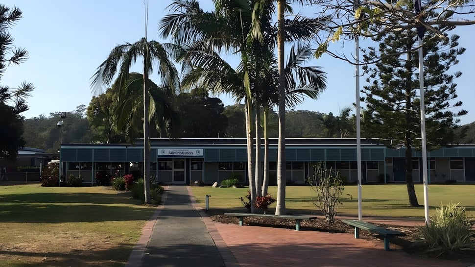 El edificio de una planta con techo verde de Elanora State High School está rodeado de palmeras y áreas verdes.