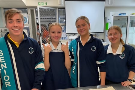 Cuatro estudiantes de Elanora State High School en uniforme escolar sonríen a la cámara en un entorno escolar.