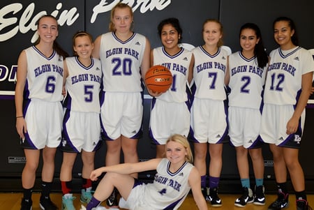 Las jugadoras de baloncesto de Elgin Park Secondary School posan juntas en sus uniformes de equipo frente al banner de la escuela.