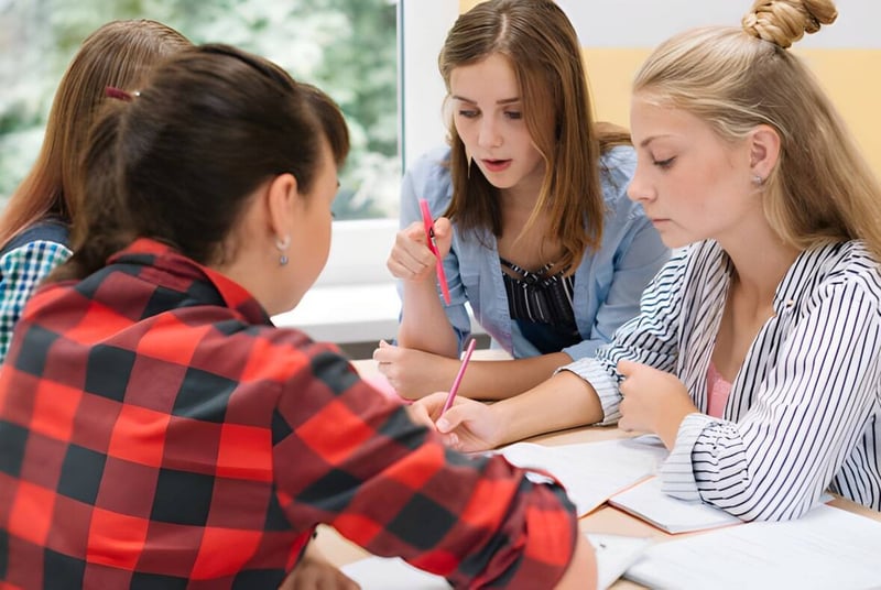 Cuatro estudiantes de la Elite Preparatory Academy llevan a cabo una discusión concentrada en un interior.