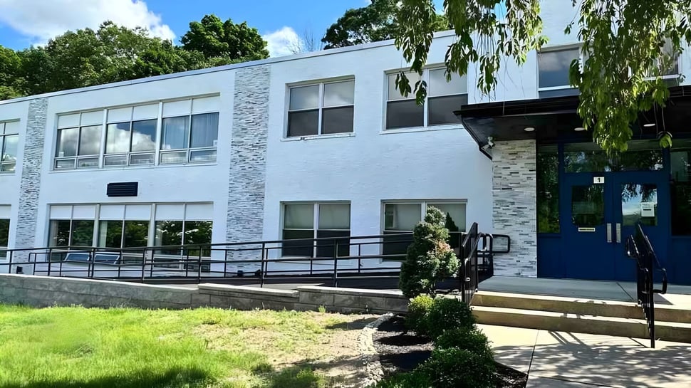 El moderno edificio de varios pisos de la Elite Preparatory Academy está rodeado de árboles verdes y un césped.