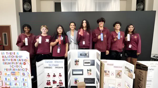 Estudiantes de la Elite Preparatory Academy presentan proyectos sobre trastornos alimentarios y rendimiento escolar ante un panel informativo.
