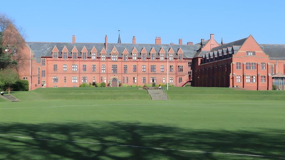 El gran edificio de ladrillo con torres y chimeneas en el campus del Ellesmere College se encuentra en un campo verde bajo un cielo despejado.