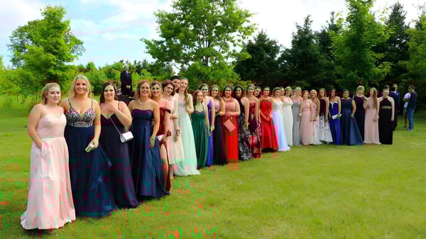 Un grupo de jóvenes mujeres en vestidos formales está de pie sobre una pradera en el terreno de la Elmvale District High School.