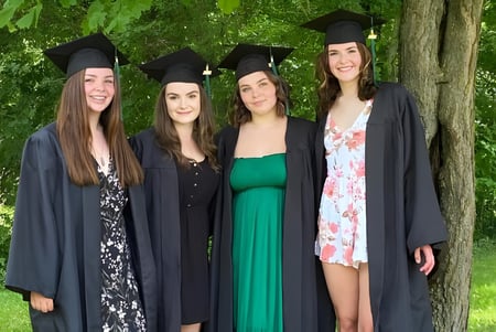 Cuatro estudiantes están vestidas con ropa de graduación en el área verde de la Elmvale District High School.