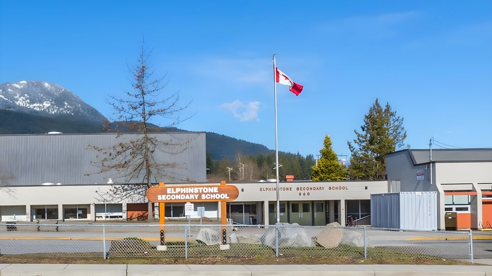 El moderno edificio de la Elphinstone Secondary School con una bandera canadiense y montañas al fondo.