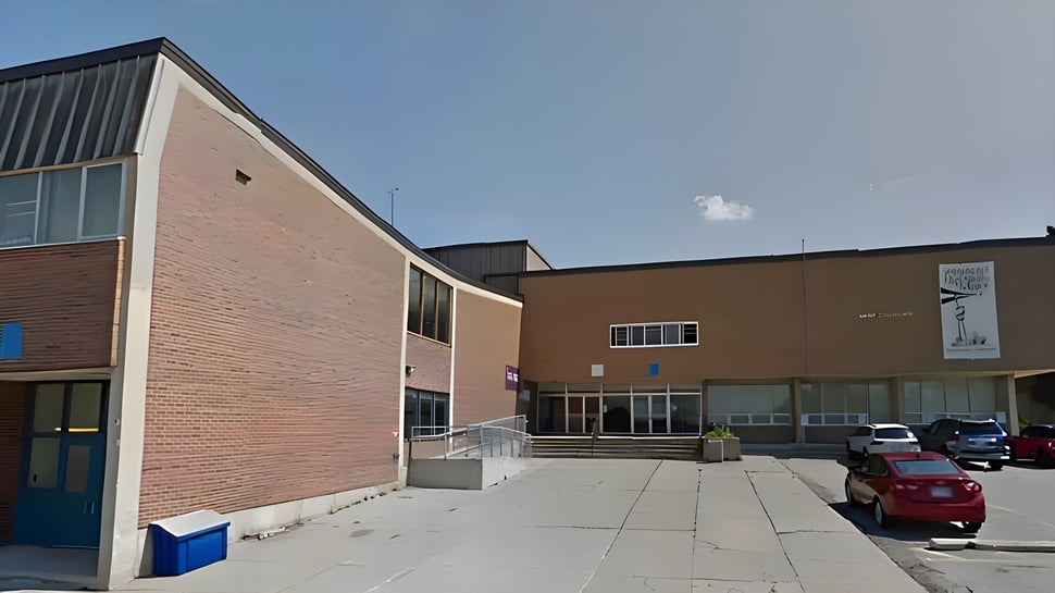 El moderno edificio de ladrillo con grandes ventanas del Emery Collegiate Institute está rodeado de un área pavimentada con coches estacionados.