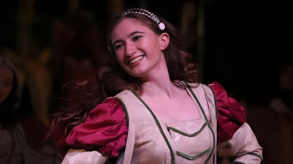 Una estudiante de la Emma Willard School con cabello rizado y cintas de perlas sonríe frente a un fondo oscuro.