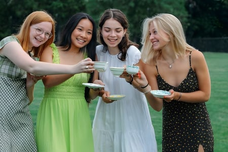 Cuatro estudiantes de la Emma Willard School están juntas al aire libre en un campo con árboles de fondo y sosteniendo bebidas.