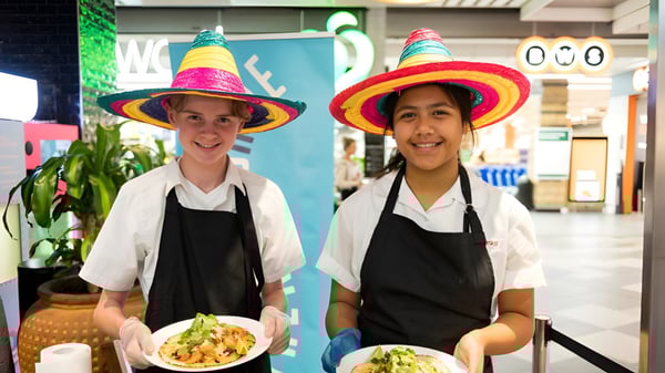 Dos personas llevan coloridos sombreros y delantales en la cocina de la Engadine High School.