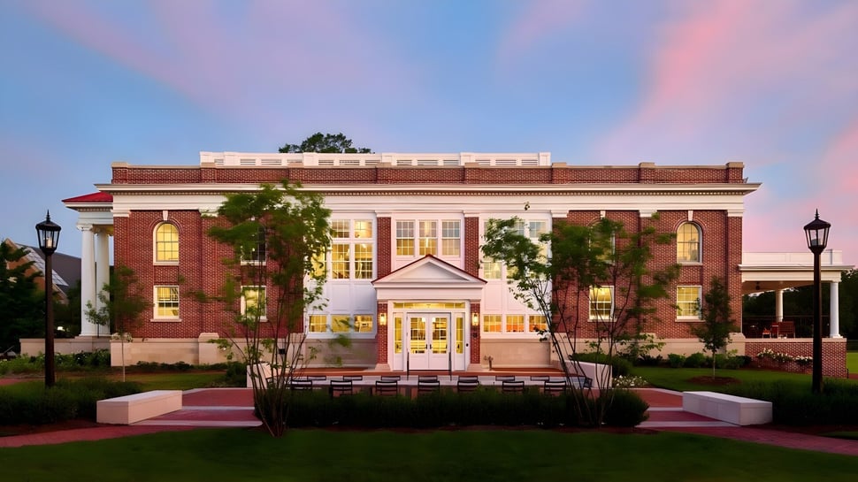 El edificio de ladrillo con entrada de columnas se encuentra en el campus de Episcopal High School y está rodeado de árboles verdes.
