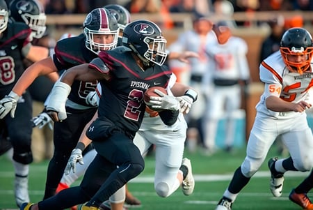 Estudiantes de Episcopal High School juegan un partido de fútbol en el campo deportivo con espectadores al fondo.