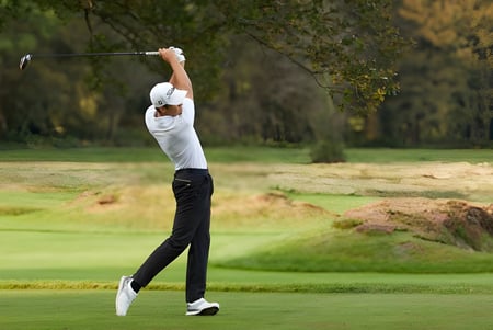 Un golfista con camisa blanca está haciendo un swing con un palo de golf en el campo de golf de Epsom College.