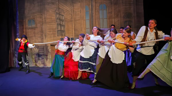 Estudiantes de Epsom College bailan con coloridos trajes tradicionales en un escenario con fondo de madera.
