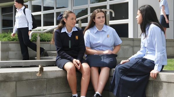 Un grupo de alumnas de la Epsom Girls Grammar School está sentada en una escalera frente al edificio escolar y conversan.