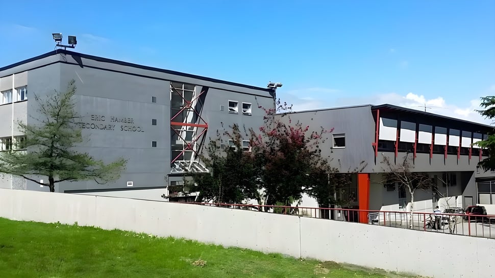 El moderno edificio de varios pisos de la Eric Hamber Secondary School con fachadas de vidrio y hormigón se encuentra en un terreno cubierto de hierba con árboles.