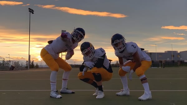 Tres jugadores de fútbol en uniforme se preparan en el campo de la Ernest Manning High School.