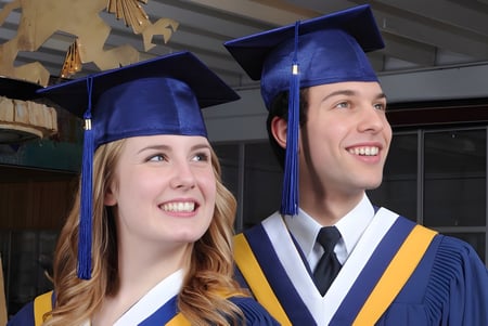 Dos graduados de la Ernest Manning High School en togas azules están en una habitación con estanterías de madera y utensilios de graduación.