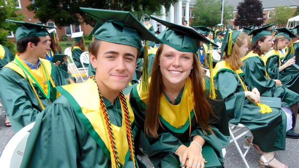 Dos graduados de la Ernestown Secondary School en togas verdes están juntos y sonríen durante la ceremonia de graduación.