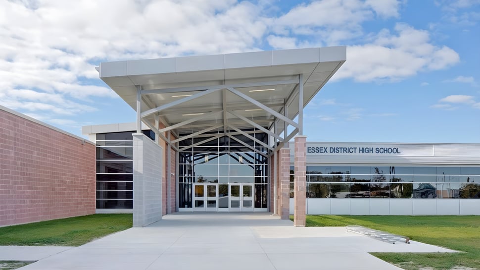 El moderno edificio escolar de Essex District High School con fachada de vidrio y arquitectura distintiva frente a un cielo azul.
