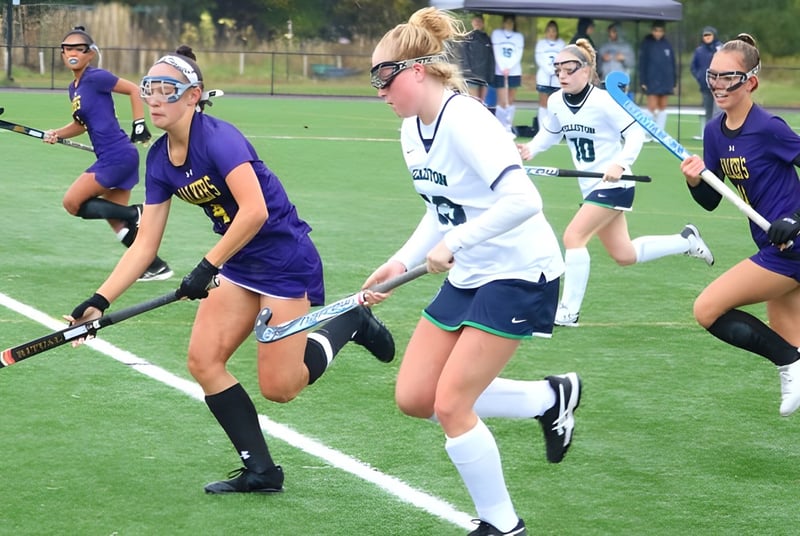 Estudiantes de la Ethel Walker School juegan un partido de hockey sobre campo en un campo de césped.