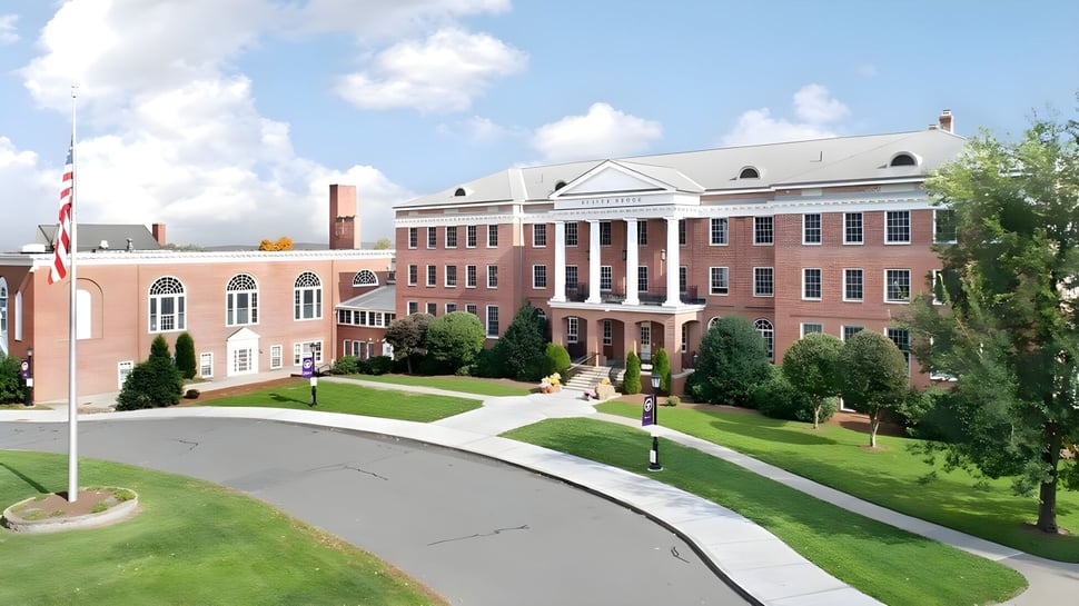 El edificio principal de la Ethel Walker School en un campus verde con árboles y un camino curvado hacia la entrada.