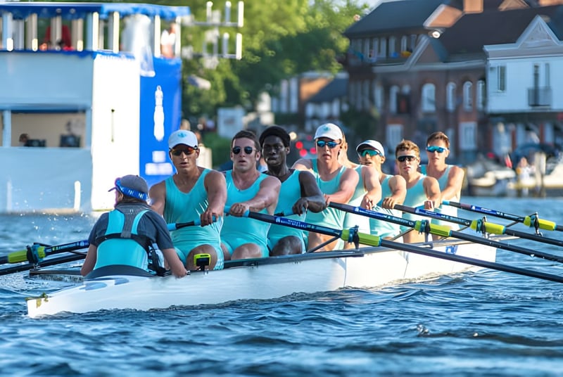 Un grupo de remeros en uniformes turquesa uniformes está sentado en el bote de remo sobre el agua frente a un paisaje pintoresco en el campus del Eton College.