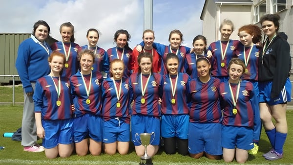 Un grupo de alumnas de la Eureka Secondary School posan juntas en camisetas azules y rojas en un campo de fútbol.