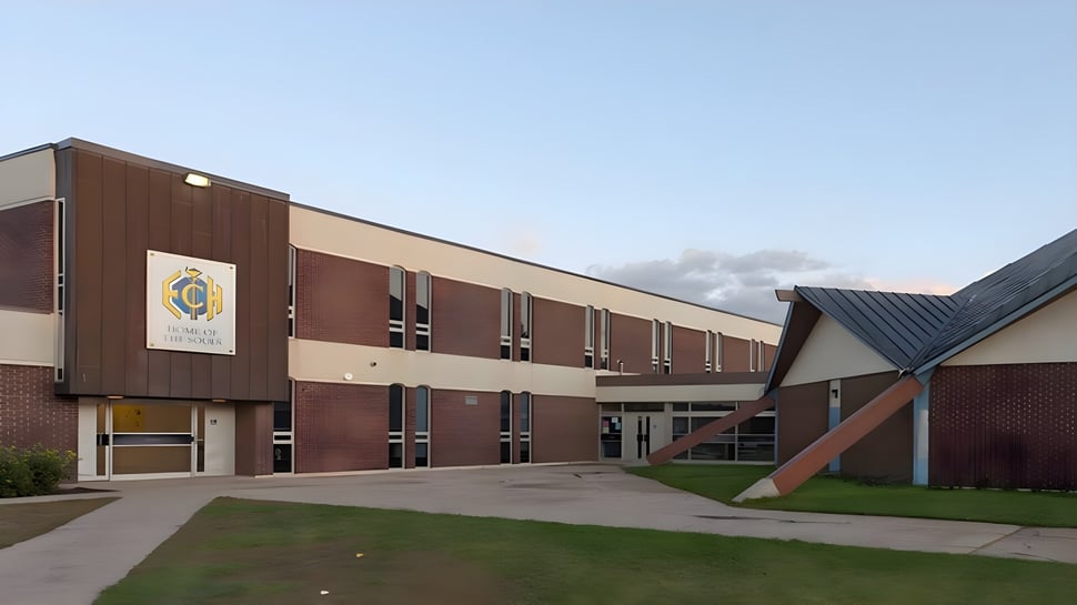 El edificio de ladrillo de varios pisos con el logo de la Evan Hardy Collegiate se encuentra en un terreno verde bajo un cielo azul.