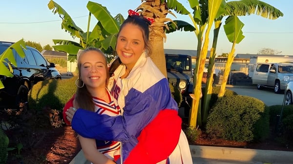 Dos mujeres se abrazan frente a plantas tropicales en el terreno de la Evangel Christian Academy.