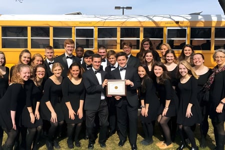 Un grupo de estudiantes de la Fabius Pompey High School posan frente a un autobús escolar amarillo.