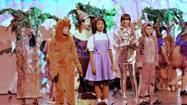 Estudiantes de la Fabius Pompey High School llevan disfraces coloridos frente a un fondo surrealista.